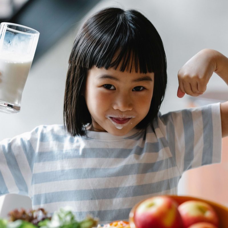 Vitamin D Benefits in Your Health - A little girl drinking milk flexes for the camera