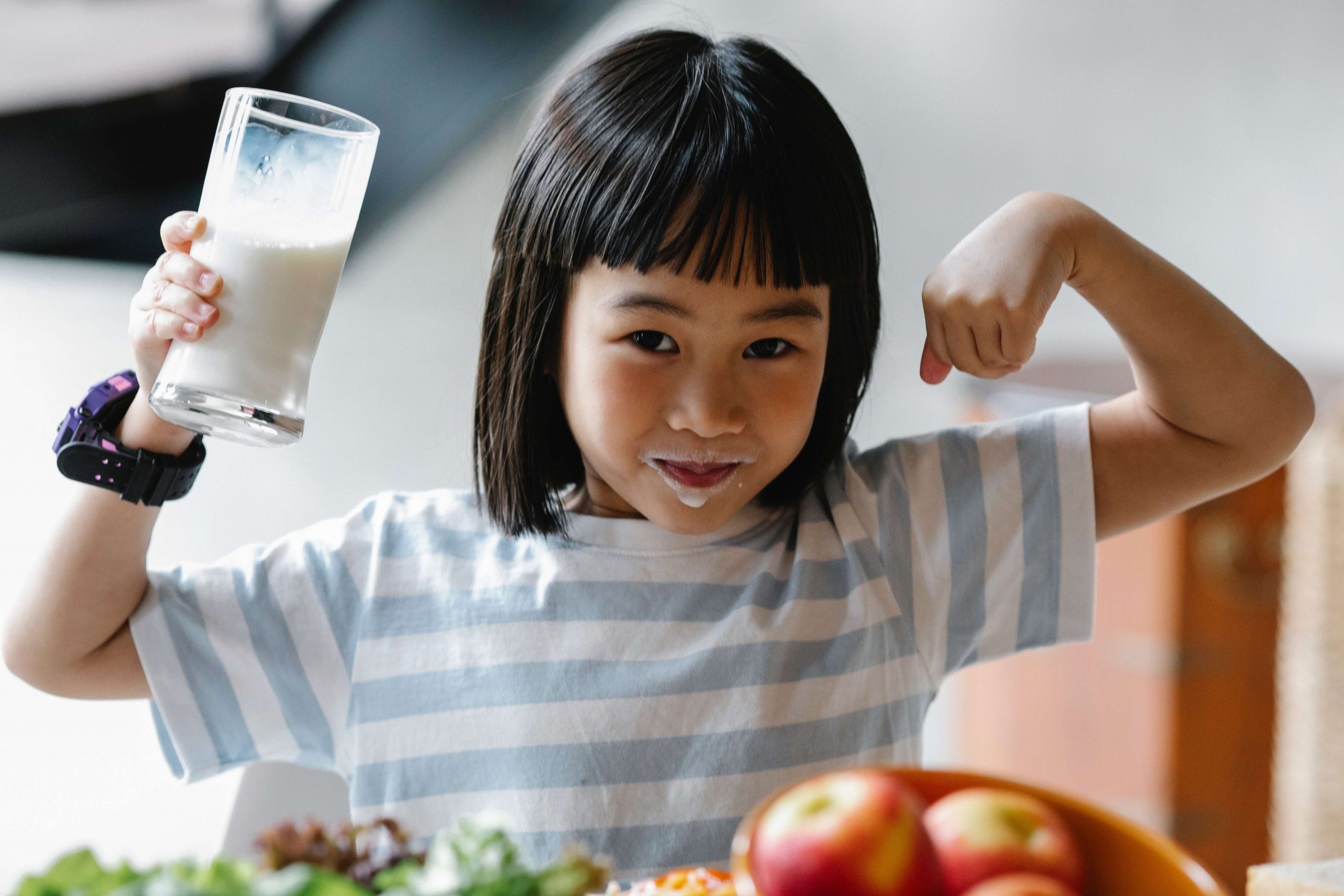 Vitamin D Benefits in Your Health - A little girl drinking milk flexes for the camera