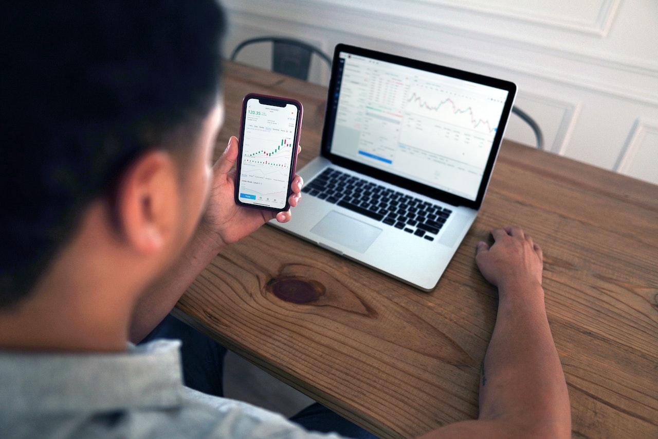 man looking at computer and phone investing money automatically