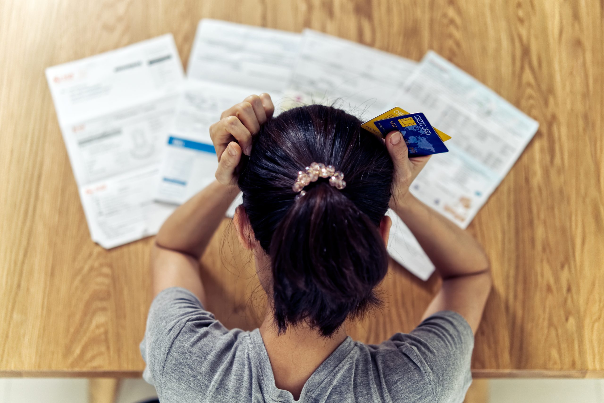 Pay Off Credit Card Debt/Top view of stressed young sitting Asian woman hands holding cards